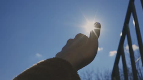 hand with thumbs up covering bright sun in the sky