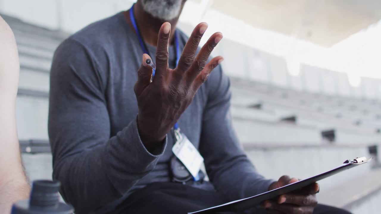 Midsection of african american male coach and caucasian male athlete sitting and talking