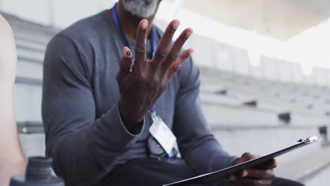 Midsection-of-african-american-male-coach-and-caucasian-male-athlete-sitting-and-talking