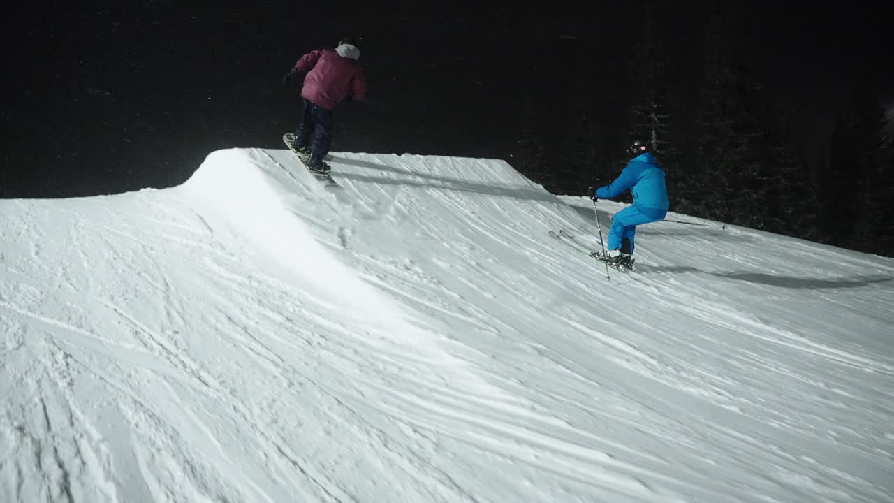 노르웨이 스키 리조트에서 어둠 속에서 눈 언덕에서 점프하는 스키어와 스노보더의 밤에 4k 슬로우 모션 추적