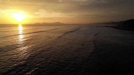 aerial tracking shows a beautiful late surf session at sunset with an island in the background on the beach of a south american city