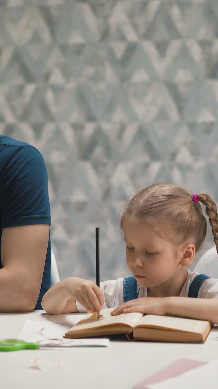 upset father talks on phone trying to work while cute blonde daughter does home task at white table with laptop in room staying home during quarantine