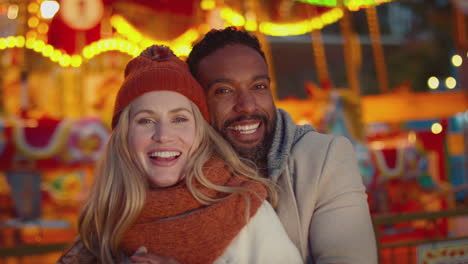 Portrait-of-couple-enjoying-on-date-in-standing-by-carousel-at-Christmas-funfair-at-night---shot-in-slow-motion