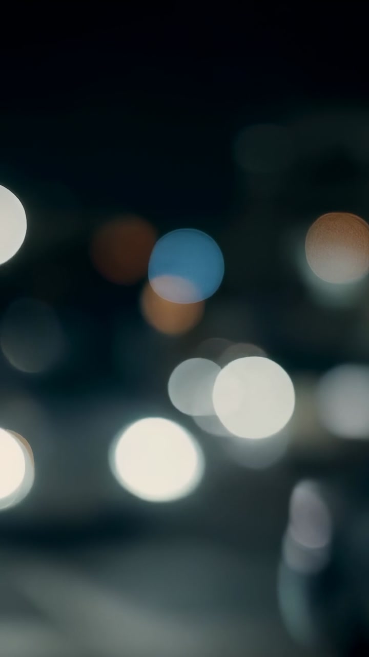 Vertical video: Camera shifting bokeh drifting bright orb rising blue-amber lights forming for film