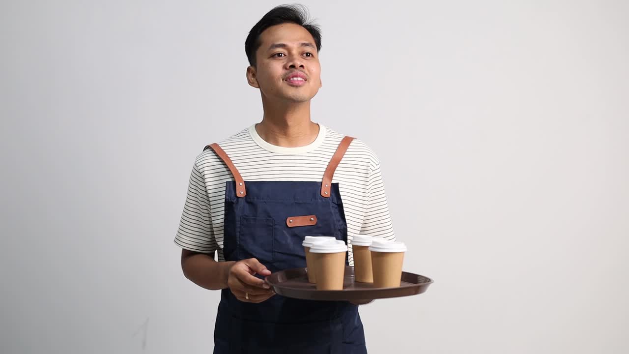 Pelayan pria membawa nampan berisi minuman, tersenyum ramah, melihat ke kiri dan kanan mencari pelanggan, dan mengantarkan pesanan minuman