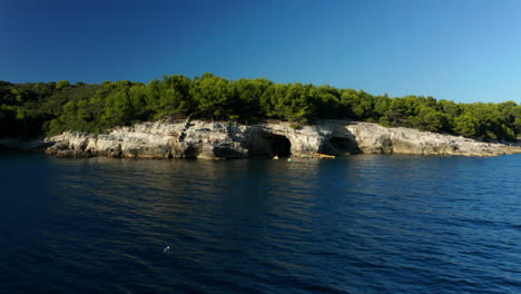 Panorama-De-La-Playa-De-Rocas-De-Gaviota-Y-Cueva-Con-Gente-En-Kayaks-En-Verano-En-Pula,-Croacia