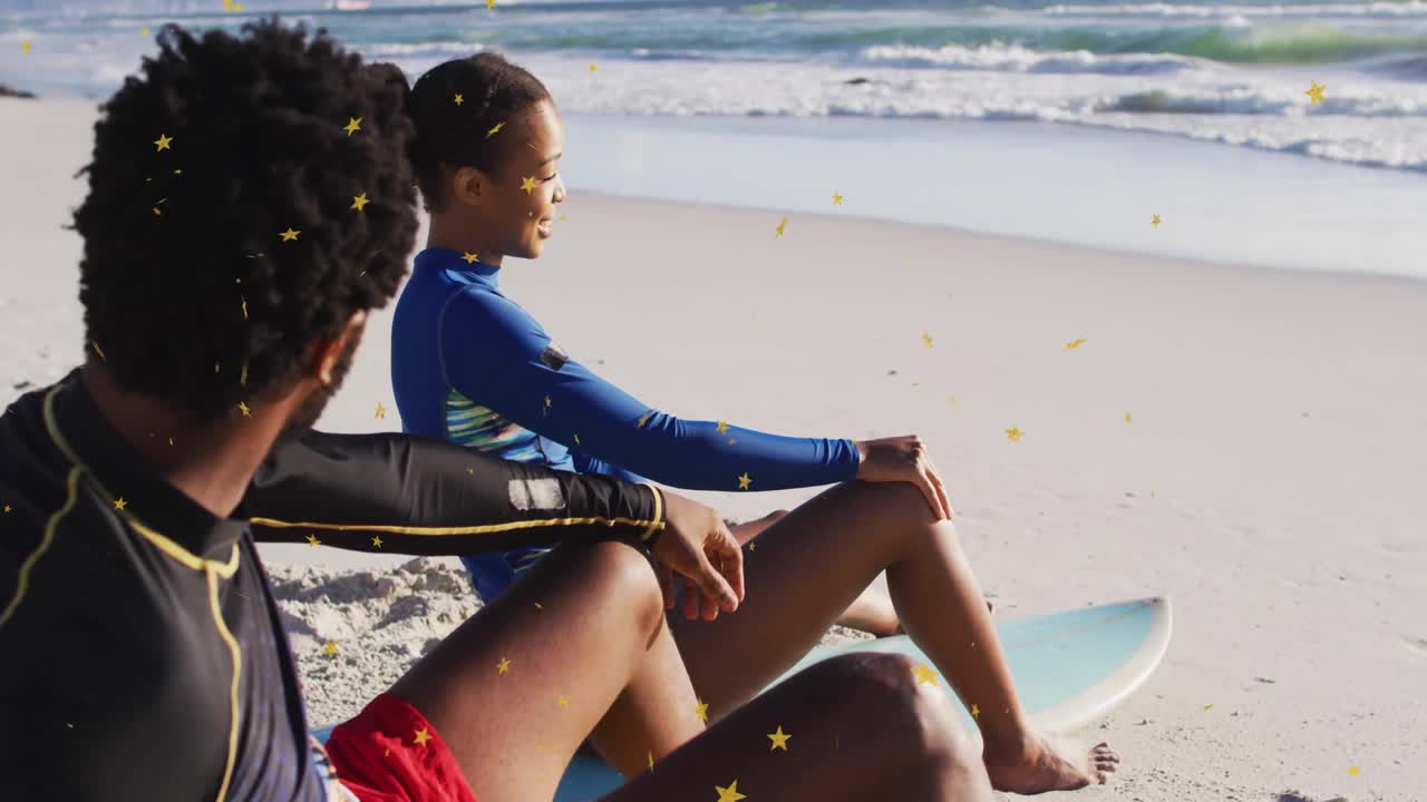 Two surfers sitting on surfboards at beach, woman pointing at incoming breakers for paddling out