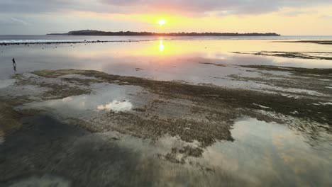 Paisaje-Paradisíaco-Aéreo-Sobrevuelo,-Pareja-Caminando-Y-Reflejo-Del-Agua-Durante-La-Puesta-De-Sol-En-El-Horizonte