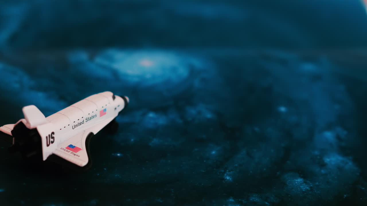 Close up of a miniature toy space shuttle placed on a blue cosmic galaxy backdrop