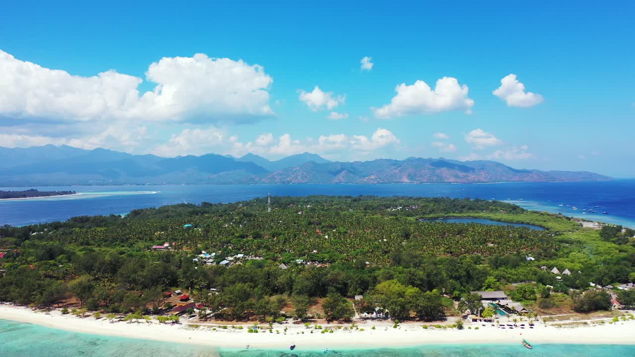 Asian tropical scenery of low island with lush vegetation and palm trees, white beach and turquoise lagoon with coral reefs on sea bottom under bright sky with white clouds in Gili Meno