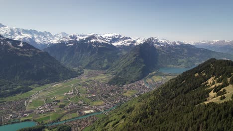 drone shot of interlaken in switzerland, with green valleys, snow-covered alps, and blue lakes under clear skies