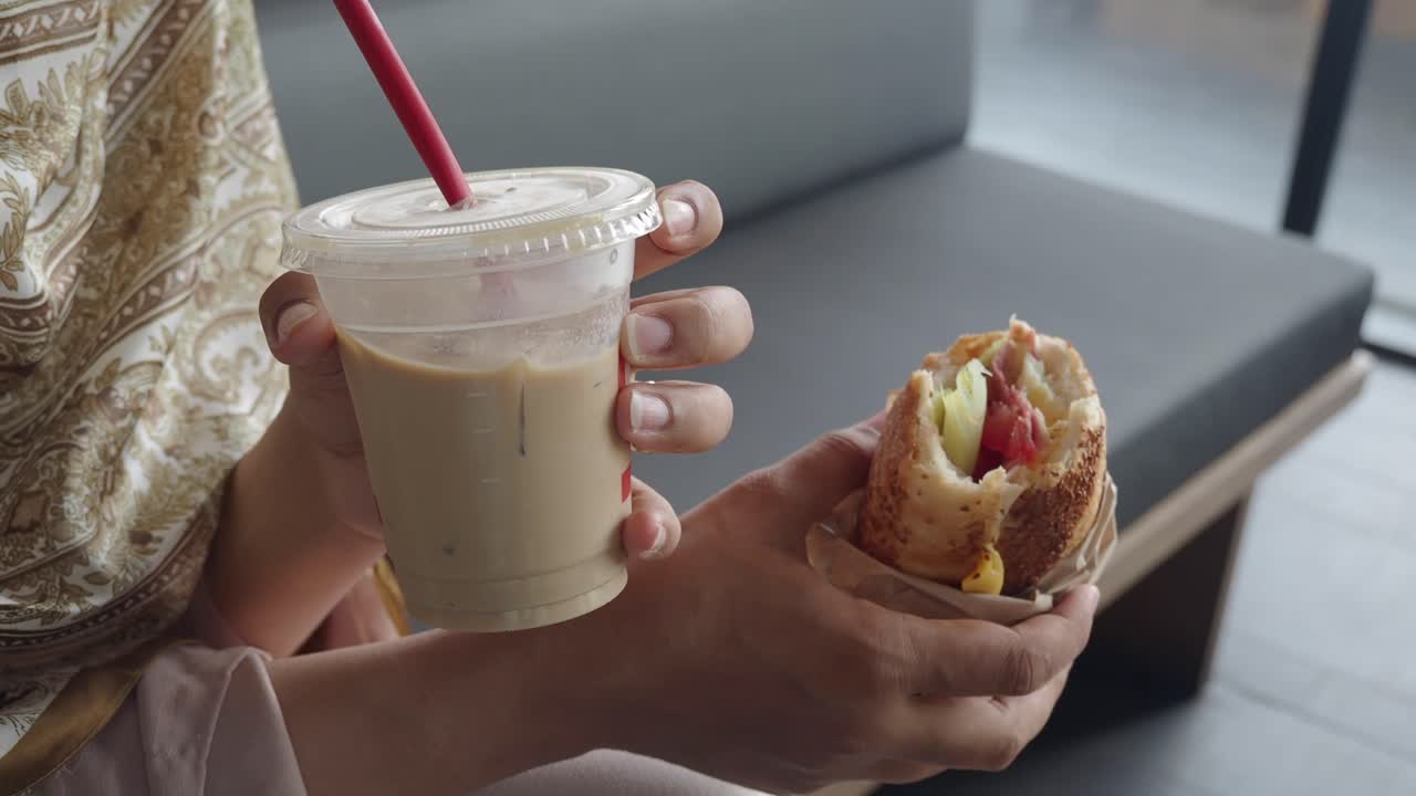 Woman eating a sandwich and drinking iced coffee
