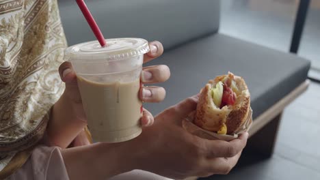 woman eating a sandwich and drinking iced coffee