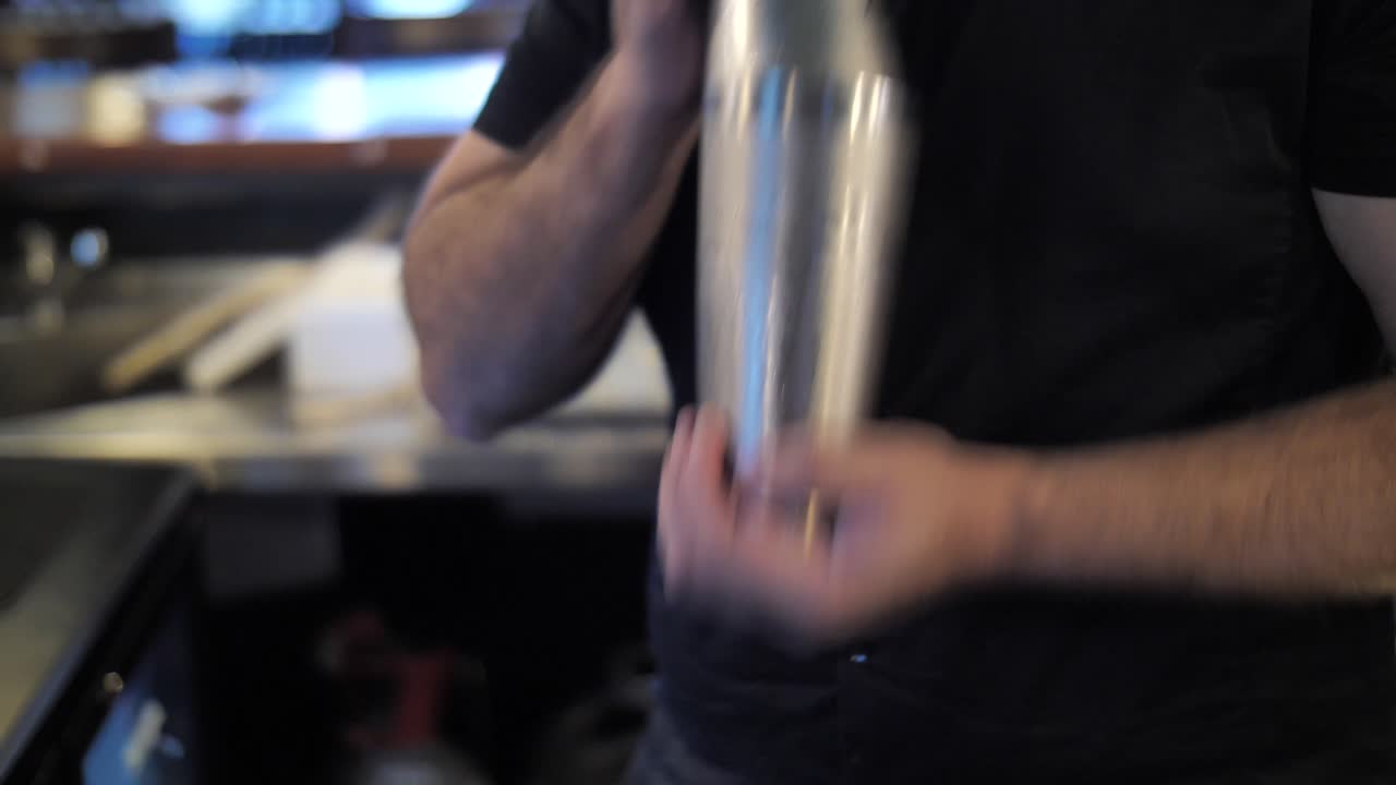 Bartender mixing drinks in shaker while making cocktails at bar counter close up