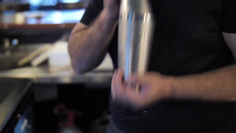 Bartender-mixing-drinks-in-shaker-while-making-cocktails-at-bar-counter-close-up