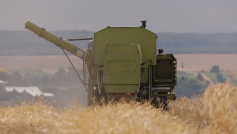 old green combine harvester in operation in a wheat field in slow motion, view from behind