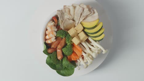 close up of a bowl of sukiyaki or shabu spinning around on the white table