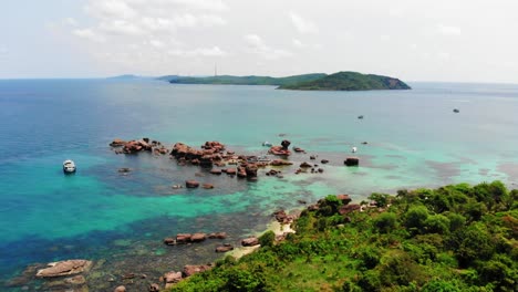 boat anchored in clear turquoise sea waters next to rocks and rocky coast of gam ghi island in vietnam archipel, phu quoc region, aerial view