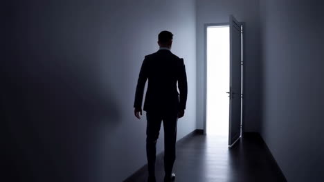 silhouette of a businessman walking towards a bright open door at the end of a dark hallway