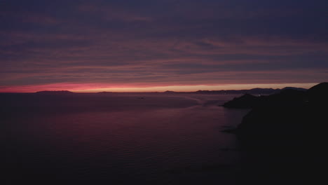 Episch-Farbenfroher-Sonnenuntergang-Mit-Einem-Schmalen-Streifen-Klaren-Himmels-In-Sehr-Weiter-Entfernung-Und-Verschiedenen-Rottönen,-Die-Sich-Auf-Der-Großen-Wolken--Und-Meeresoberfläche-Widerspiegeln