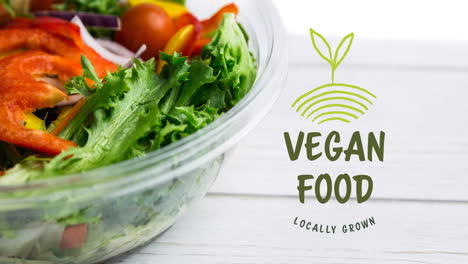 animation of vegan food text in green over fresh organic vegetable salad in bowl on wooden boards