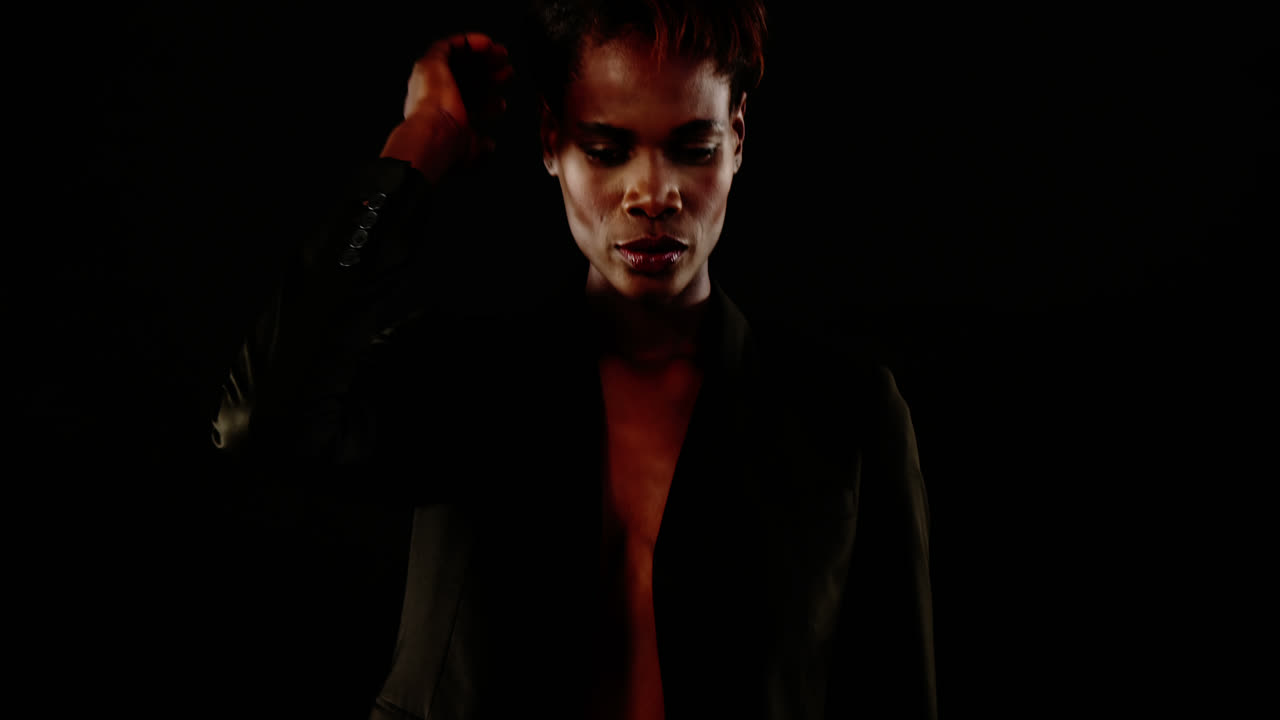 андрогинный мужчина в блейзере позирует на черном фоне