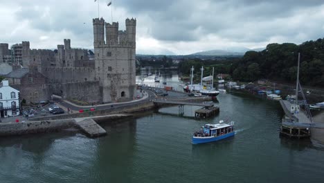 sightseeing boat sailing caernarfon castle welsh harbour town river aerial view descending pull back