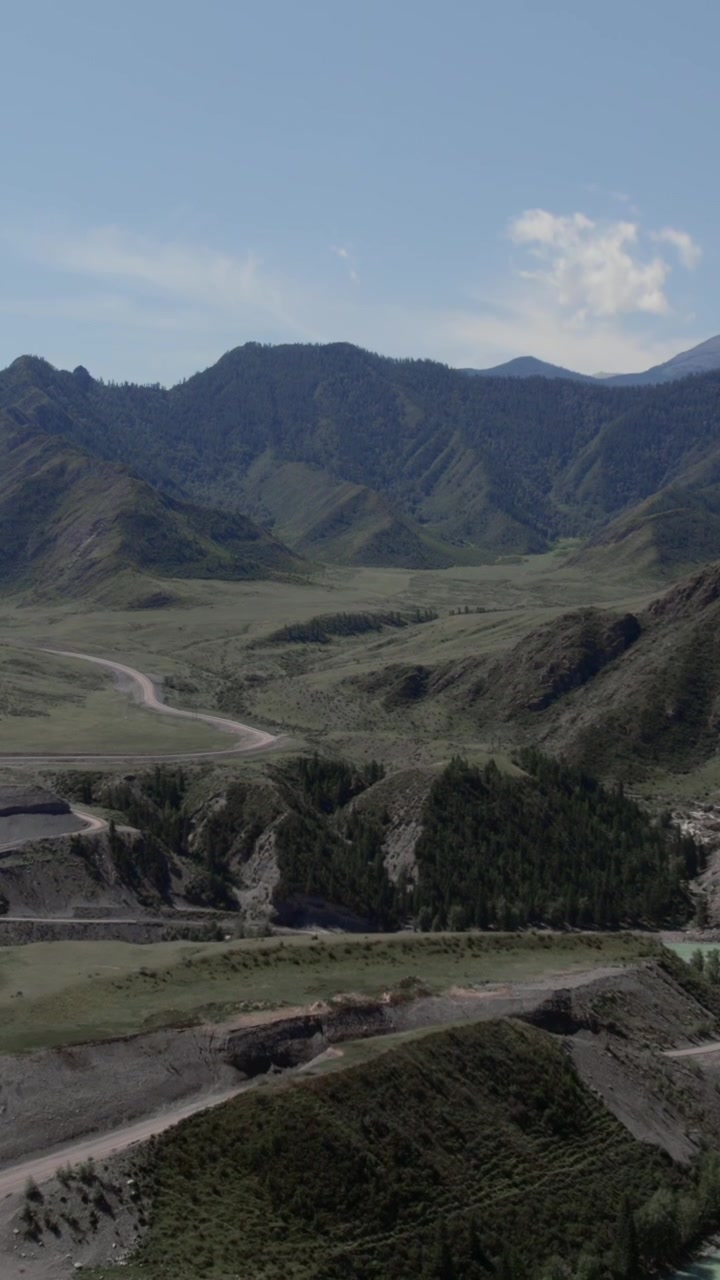 Riprese aeree della Chuysky Trakt che si snoda attraverso un'ampia valle verde e montagne boscose nella Repubblica dell'Altai, Russia, con cielo sereno e natura selvaggia remota.