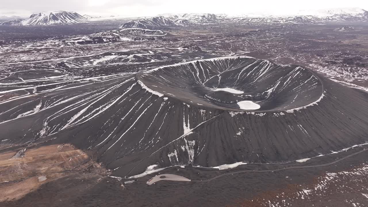 Aerial view of the snow-streaked Hverfjall volcanic crater near Lake Mývatn in Iceland, highlighting the symmetrical shape and rugged lava field surroundings.