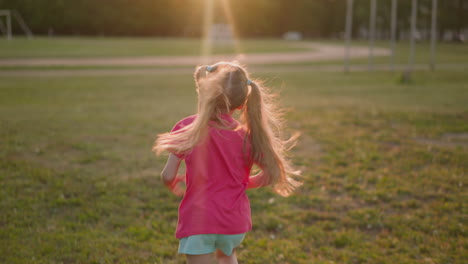 Little-girl-with-blonde-ponytails-runs-along-green-field