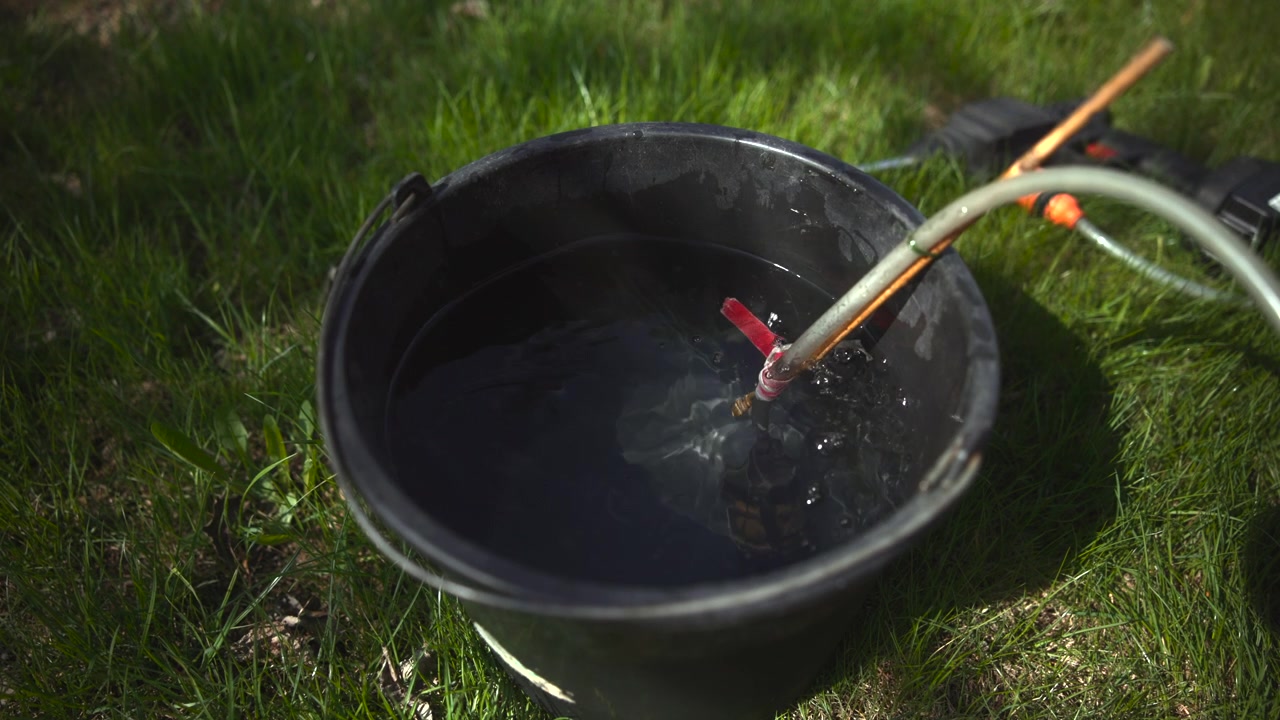 Een zwarte plastic emmer gevuld met water staat 's nachts op een grasveld, verlicht door een sterk gericht licht dat heldere reflecties en diepe schaduwen creëert.