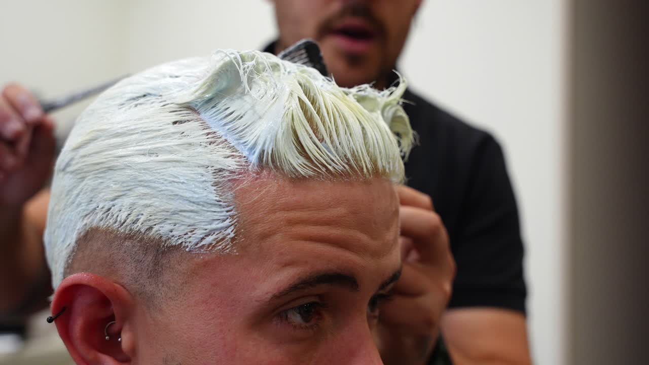 Tight close-up of hairdresser using comb to separate sections where bleaching powder is already applied