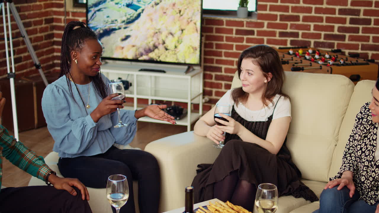Happy women chatting on cozy couch at apartment party, drinking wine and enjoying conversation