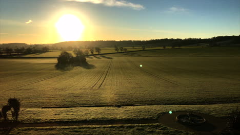 Leicestershire-Herrenhaus-Mit-Blick-Auf-Den-Sonnenaufgang-Auf-Einem-Grünen-Und-Goldenen-Feld-Und-Einem-Blauen-Himmel-Dahinter,-Der-Eine-Silhouette-über-Einer-Koppel-Schafft