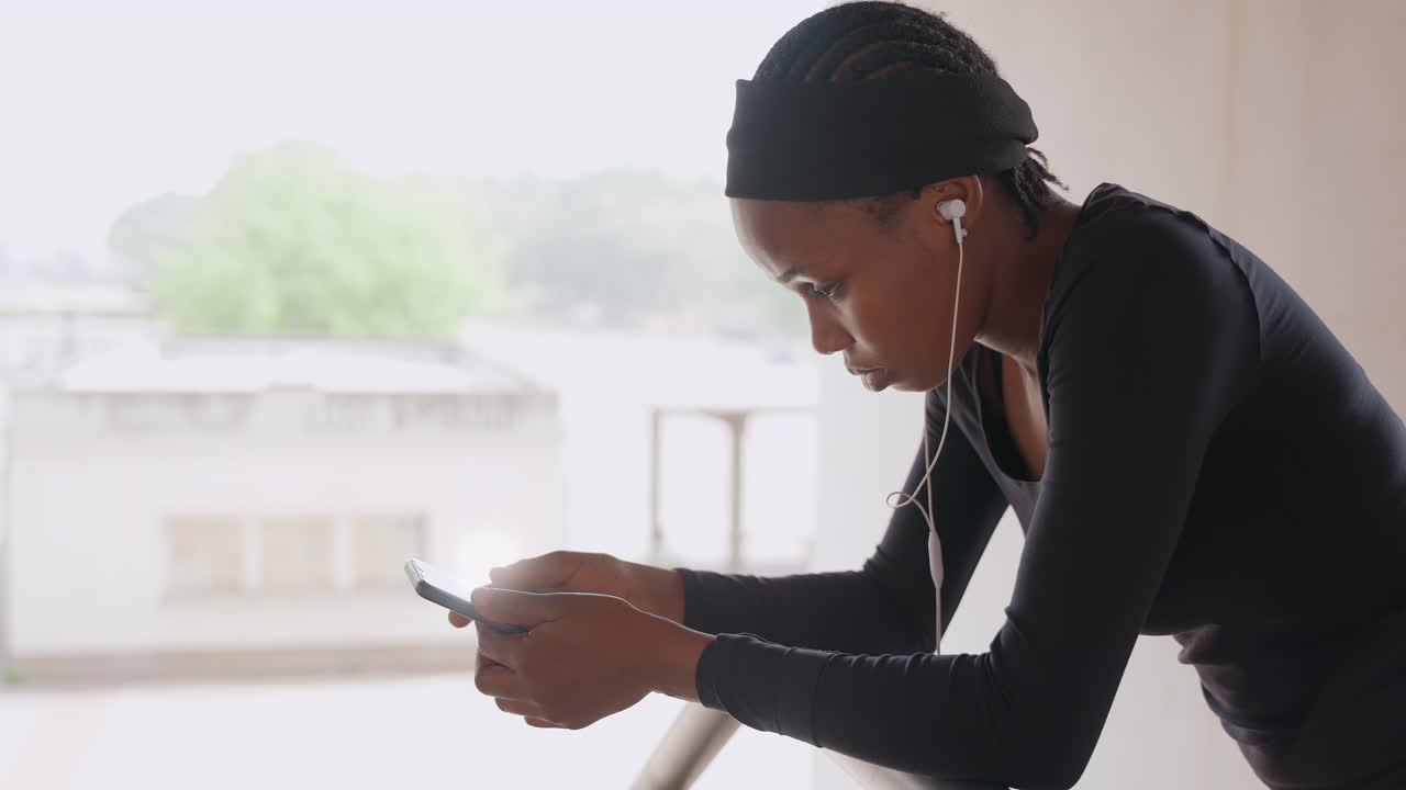 Una donna esamina la sua lista musicale prima di una sessione di esercizi. L'atleta controlla con concentrazione le sue tracce per l'allenamento. Una donna determinata studia la sua playlist con uno sfondo di delicato paesaggio urbano.