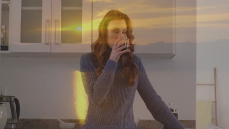 Animation-of-sunset-landscape-over-caucasian-woman-drinking-coffee-in-kitchen