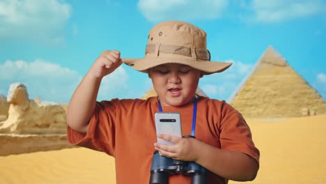 boy explorer with smartphone and binoculars in front of pyramids