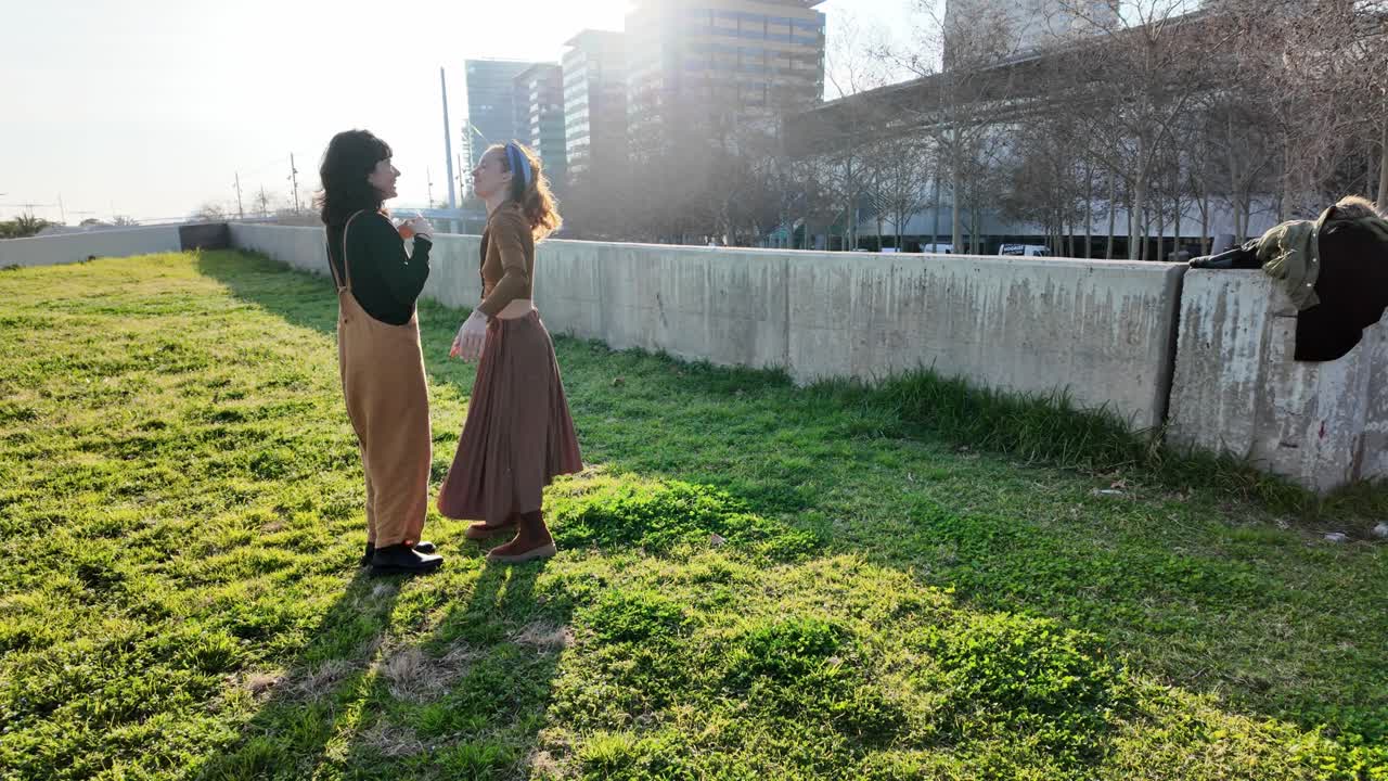 Two women embracing in a park in an urban setting