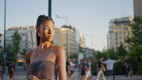 mujer de piel oscura caminando por la ciudad del sol en primer plano. modelo de moda con teléfono inteligente
