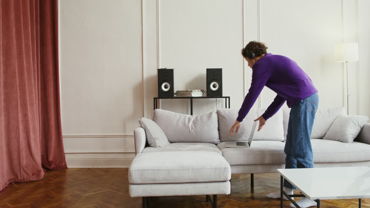 현대적인 거실에서 노트북과 헤드폰을 들고 소파에서 휴식을 취하는 남자.