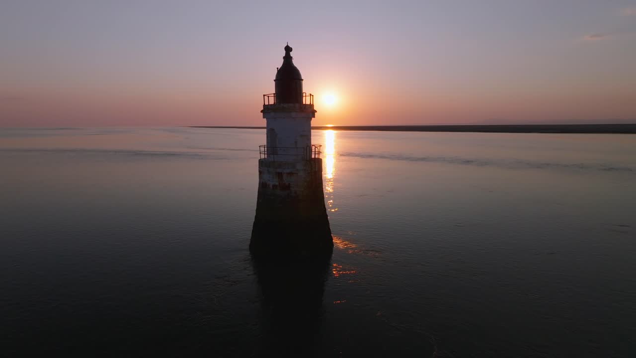 Abandoned derelict lighthouse occluding the setting sun in very calm waters. Plover Scar Lighthouse, Lancashire, UK.