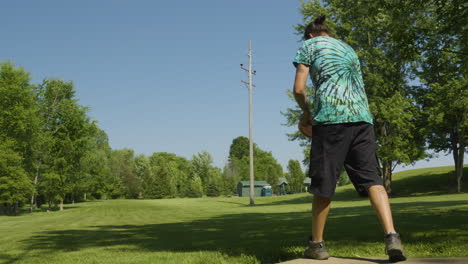 Un-Hombre-Lanza-Un-Disco-Durante-Un-Juego-De-Disc-Golf-En-Un-Parque-Verde,-Capturando-La-Energía-Y-El-Enfoque-Del-Deporte