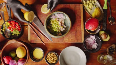 Preparación-De-Ceviche---Vista-Superior-De-La-Mesa-De-Un-Chef-Profesional-Cortando-El-Limón-Por-La-Mitad-Y-Exprimiéndolo-En-Un-Tazón-De-Ingredientes-Frescos,-Dando-Al-Plato-Un-Concepto-De-Escena-De-Cocina-Cítrica