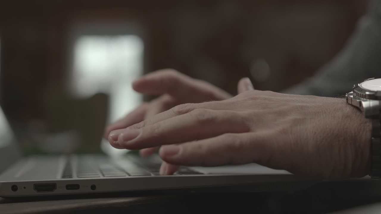 Businessman with wristwatch writes email on laptop in office