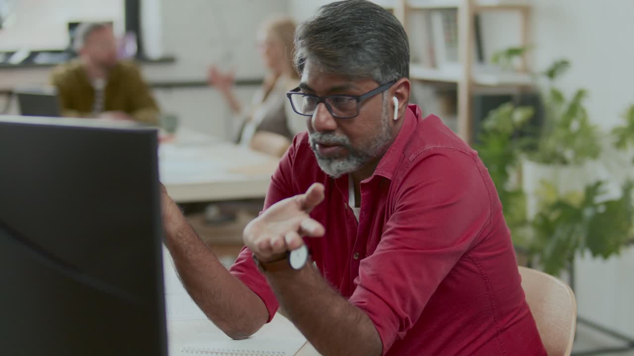 Indian Businessman in Earphones Talking via Video Call on Computer in Office
