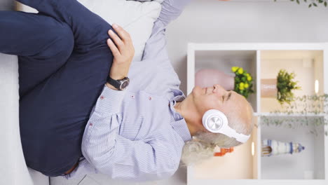 Vertical-video-of-Unhappy-old-man-listening-to-music-with-headphones.