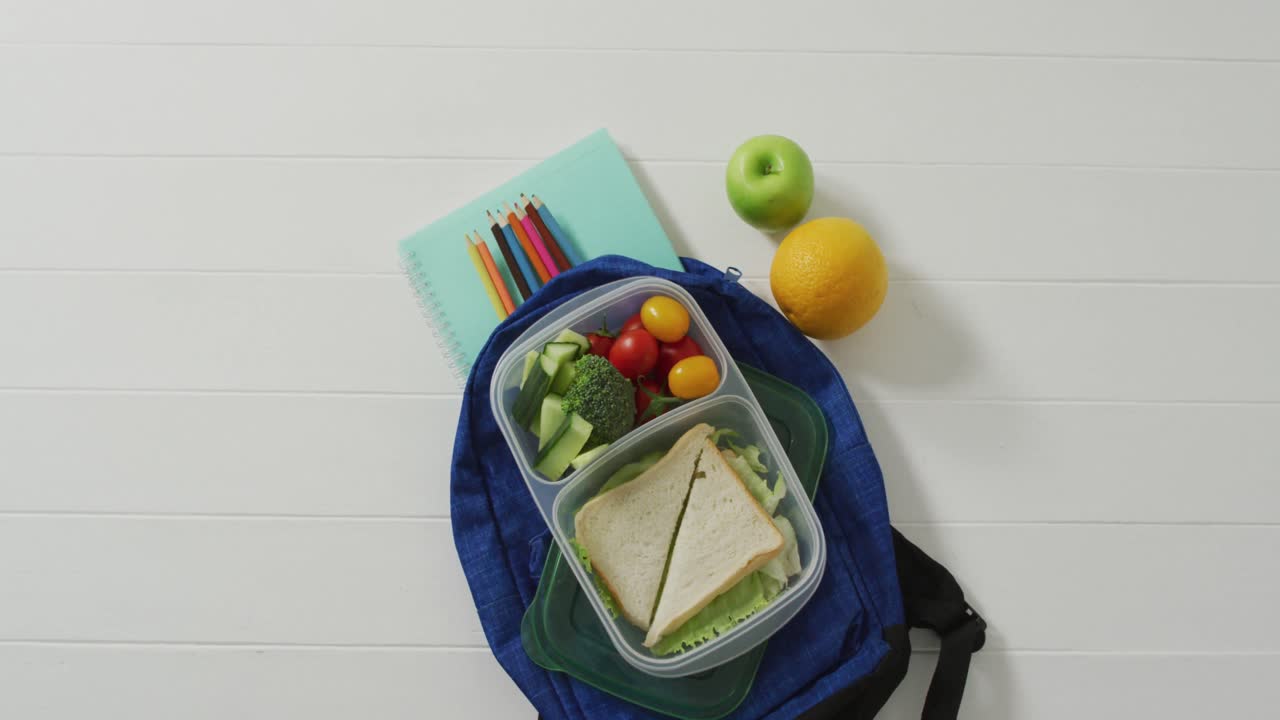 vídeo de un almuerzo sano envasado de frutas y verduras, con lápices de colores en el bolso escolar