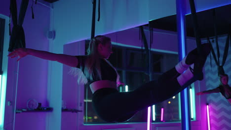 una mujer hace yoga deportivo en el aire en una hamaca a la luz del neón realizando ejercicios y movimientos graciosos de estiramiento y baile en cámara lenta.