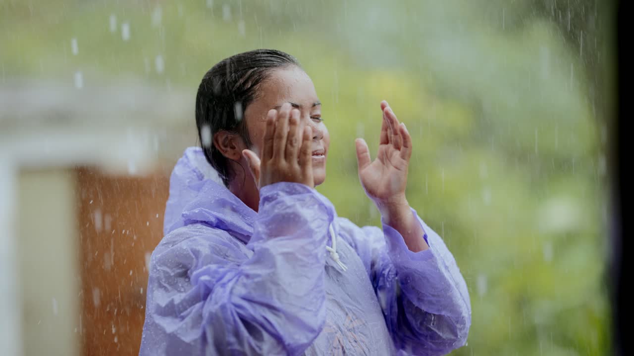 Cheerful Indian village child enjoying rainy weather in bright raincoat, rural lifestyle moment, 4k video