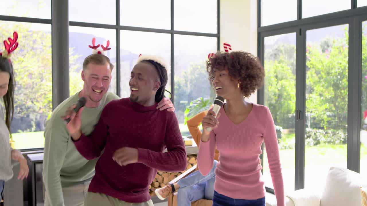 Diverse friends singing karaoke after Black man stepping center holding mic by Xmas tree in room